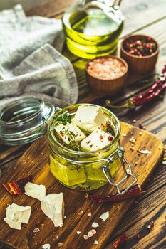 Feta cheese marinated in olive oil with fresh herbs in glass jar. Wooden background
