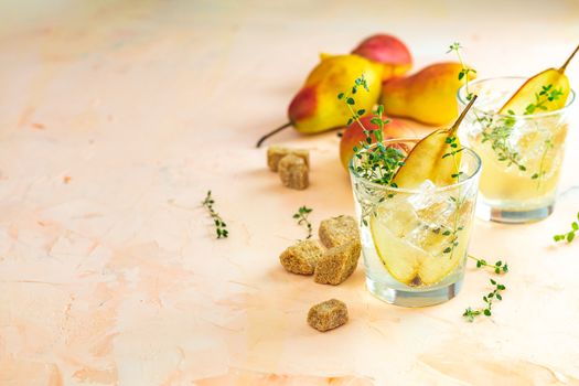 Cold pear white tea with thyme on the pink concrete table background. Festive summer drinks, pear thyme cocktail. Selective focus, space for text
