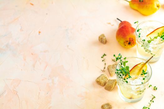 Cold pear white tea with thyme on the pink concrete table background. Festive summer drinks, pear thyme cocktail. Selective focus, space for text