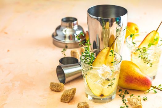 Cold pear white tea with thyme on the pink concrete table background. Festive summer drinks, pear thyme cocktail. Selective focus, space for text