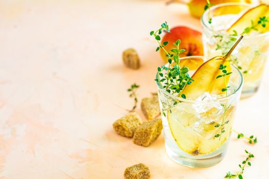 Cold pear white tea with thyme on the pink concrete table background. Festive summer drinks, pear thyme cocktail. Selective focus, space for text