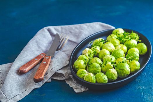 Fresh organic Brussels sprouts in served on black plate, dark blue concrete table surface, copy space for you text.