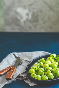 Fresh organic Brussels sprouts in served on black plate, dark blue concrete table surface, copy space for you text.