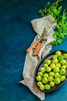 Fresh organic Brussels sprouts in served on black plate, dark blue concrete table surface, copy space for you text.