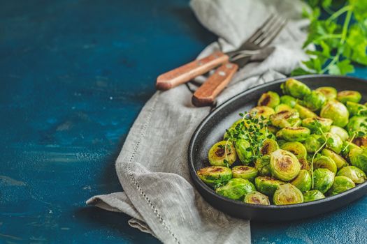 Black plate with delicious roasted Brussels sprouts in served on black plate, dark blue concrete table surface, copy space for you text.