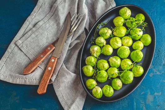 Fresh organic Brussels sprouts in served on black plate, dark blue concrete table surface, copy space for you text.