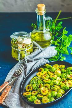 Black plate with delicious roasted Brussels sprouts in served on black plate, dark blue concrete table surface, copy space for you text.