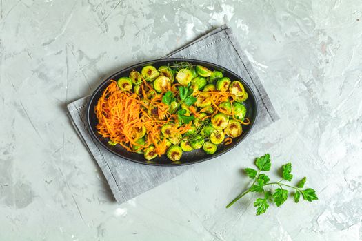 Delicious roasted Brussels sprouts and marinated carrot chips in served on black plate, light gray concrete table surface, top view, copy space for you text.