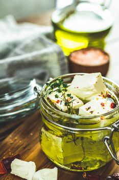 Feta cheese marinated in olive oil with fresh herbs in glass jar. Wooden background.