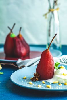 Pears in wine. Traditional dessert pears stewed in red wine with wine sauce on plate on blue concrete surface. Concept for romantic dinner dessert