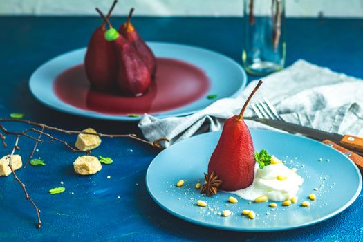 Pears in wine. Traditional dessert pears stewed in red wine with wine sauce on plate on blue concrete surface. Concept for romantic dinner dessert