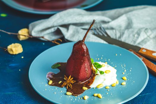 Pears in wine. Traditional dessert pears stewed in red wine with chocolate sauce on plate on blue concrete surface. Concept for romantic dinner dessert