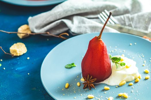 Pears in wine. Traditional dessert pears stewed in red wine with wine sauce on plate on blue concrete surface. Concept for romantic dinner dessert