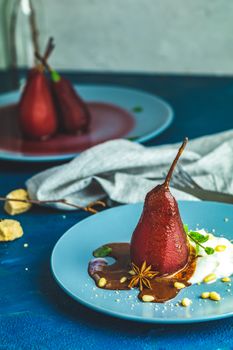 Pears in wine. Traditional dessert pears stewed in red wine with chocolate sauce on plate on blue concrete surface. Concept for romantic dinner dessert