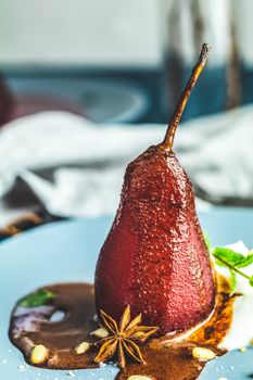 Pears in wine. Traditional dessert pears stewed in red wine with chocolate sauce on plate on blue concrete surface. Concept for romantic dinner dessert