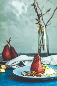 Pears in wine. Traditional dessert pears stewed in red wine with chocolate sauce on plate on blue concrete surface. Concept for romantic dinner dessert