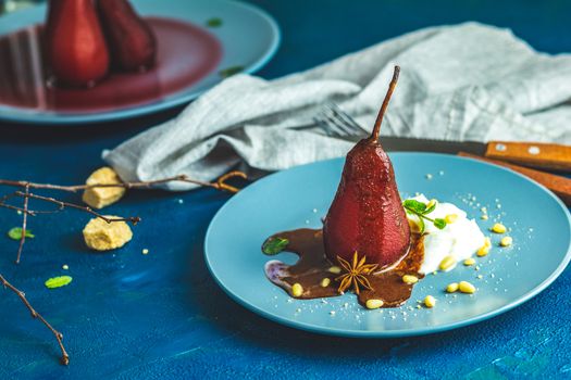 Pears in wine. Traditional dessert pears stewed in red wine with chocolate sauce on plate on blue concrete surface. Concept for romantic dinner dessert