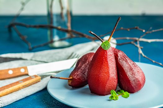 Pears in wine. Traditional dessert pears stewed in red wine with chocolate sauce on plate on blue concrete surface. Concept for romantic dinner dessert. Simple Paleo style dessert pear poached in pomegranate juice.