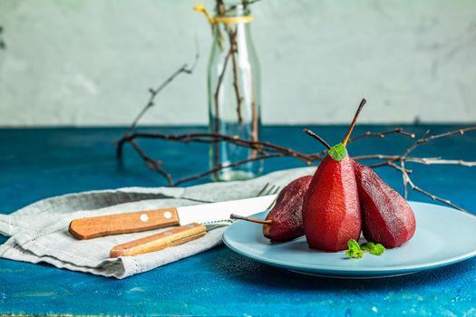 Traditional dessert pears stewed in red wine with chocolate sauce on plate on blue concrete surface. Concept for romantic dinner dessert. Simple Paleo style dessert pear poached in pomegranate juice