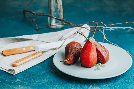 Pears in wine. Traditional dessert pears stewed in red wine with chocolate sauce on plate on blue concrete surface. Concept for romantic dinner dessert. Simple Paleo style dessert pear