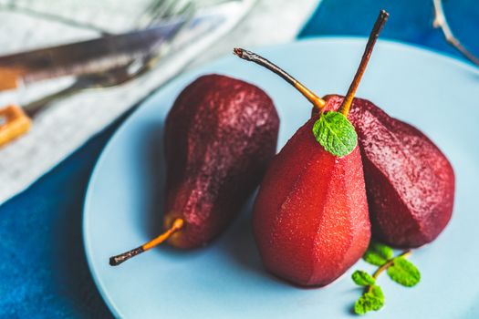 Pears in wine. Traditional dessert pears stewed in red wine with chocolate sauce on plate on blue concrete surface. Concept for romantic dinner dessert. Simple Paleo style dessert pear