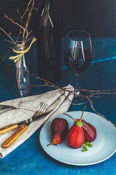 Pears in wine. Traditional dessert pears stewed in red wine with chocolate sauce on plate on blue concrete surface. Concept for romantic dinner dessert. Simple Paleo style dessert pear poached in pomegranate juice.