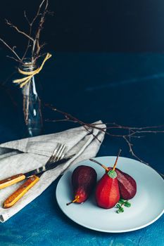 Pears in wine. Traditional dessert pears stewed in red wine with chocolate sauce on plate on blue concrete surface. Concept for romantic dinner dessert. Simple Paleo style dessert pear