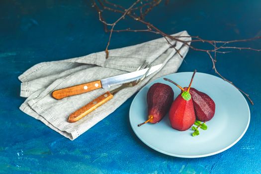 Pears in wine. Traditional dessert pears stewed in red wine with chocolate sauce on plate on blue concrete surface. Concept for romantic dinner dessert. Simple Paleo style dessert pear