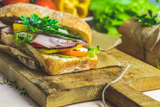 Italian porchetta sandwich. Ciabatta sandwich with ham, tomato, cheese, pepper, onion and salad on wooden cutting board with ingredients.