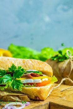 Italian porchetta sandwich. Ciabatta sandwich with ham, tomato, cheese, pepper, onion and salad on wooden cutting board with ingredients.