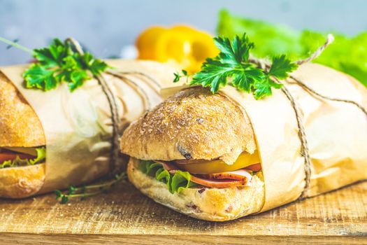 Ciabatta sandwich with ham, tomato, cheese, pepper, onion and salad on wooden cutting board with ingredients.