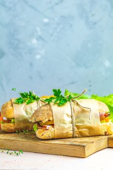 Ciabatta sandwich with ham, tomato, cheese, pepper, onion and salad on wooden cutting board with ingredients.