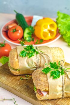 Italian porchetta sandwich. Ciabatta sandwich with ham, tomato, cheese, pepper, onion and salad on wooden cutting board with ingredients.