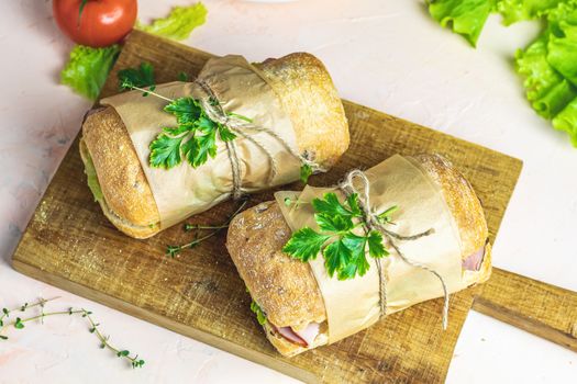 Italian porchetta sandwich. Ciabatta sandwich with ham, tomato, cheese, pepper, onion and salad on wooden cutting board with ingredients.