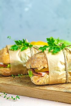 Italian porchetta sandwich. Ciabatta sandwich with ham, tomato, cheese, pepper, onion and salad on wooden cutting board with ingredients.