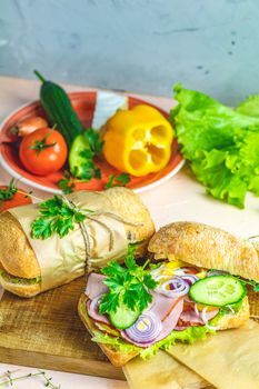 Italian porchetta sandwich. Ciabatta sandwich with ham, tomato, cheese, pepper, onion and salad on wooden cutting board with ingredients.