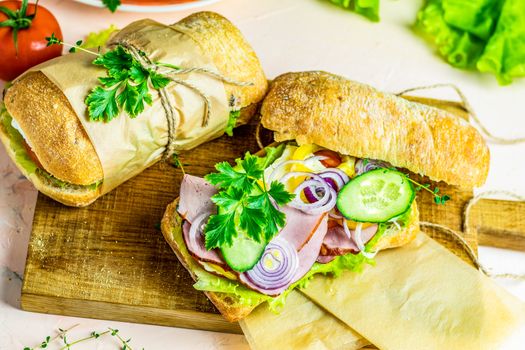 Italian porchetta sandwich. Ciabatta sandwich with ham, tomato, cheese, pepper, onion and salad on wooden cutting board with ingredients.