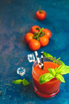 Tomato juice, red cocktail with tomato juice between tomatoes, fresh basil and ice. Delicious tomato bloody mary cocktail on dark blue concrete table.