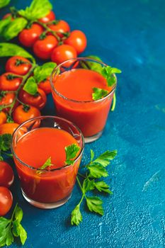 Tomato juice, red cocktail with tomato juice between tomatoes, fresh basil and ice. Delicious tomato bloody mary cocktail on dark blue concrete table.