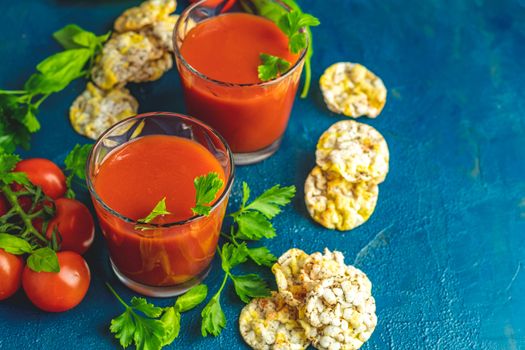 Red cocktail with tomato juice between tomatoes, basil, parsley and nutritious cereal breads. Delicious tomato bloody mary cocktail on dark blue concrete table.