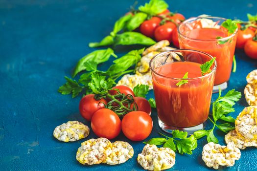 Red cocktail with tomato juice between tomatoes, basil, parsley and nutritious cereal breads. Delicious tomato bloody mary cocktail on dark blue concrete table.