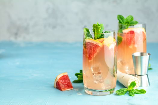 Grapefruit and fresh mint cocktail with juice, cold summer citrus refreshing drink gin tonic cocktail or beverage with ice on blue concrete surface.