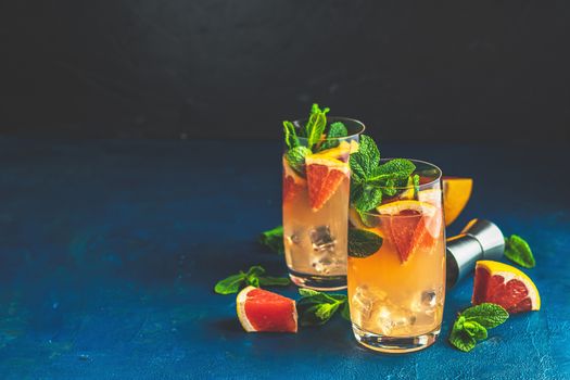 Grapefruit and mint gin tonic cocktail, refreshing drink with ice. Cold summer citrus refreshing drink cocktail or beverage with ice on dark blue concrete surface close up.
