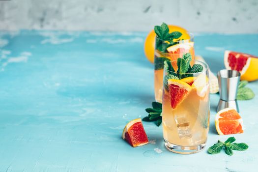 Grapefruit and fresh mint cocktail with juice, cold summer citrus refreshing drink gin tonic cocktail or beverage with ice on blue concrete surface.