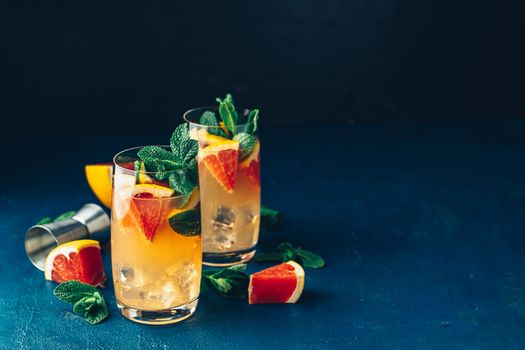 Grapefruit and fresh mint cocktail with juice, cold summer citrus refreshing drink gin tonic cocktail or beverage with ice on dark blue concrete surface.
