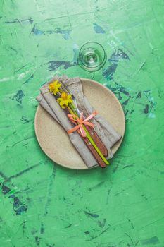 Empty beige plate and cutlery with daffodils on a napkin. Top view, green concrete surface background, copy space for you text