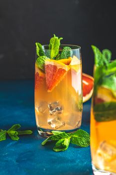 Grapefruit and mint gin tonic cocktail, refreshing drink with ice. Cold summer citrus refreshing drink cocktail or beverage with ice on dark blue concrete surface close up.