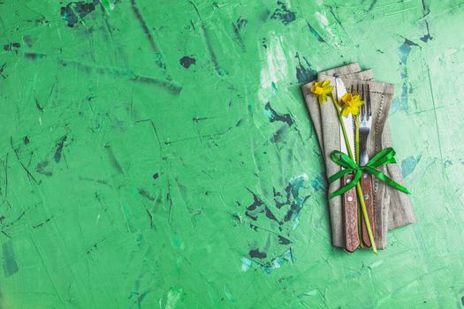 Cutlery with daffodils on a napkin. Top view, green concrete surface background, copy space for you text