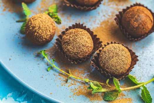 Cocoa balls, handmade chocolate balls cakes in a blue tray, sprinkled with cocoa powder, fresh mint and thyme on dark blue concrete surface background. Close up, copy space, shallow depth of the field