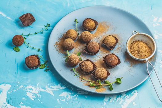 Cocoa balls, handmade chocolate balls cakes in a blue tray, sprinkled with cocoa powder, fresh mint and thyme on dark blue concrete surface background. Close up, copy space, shallow depth of the field